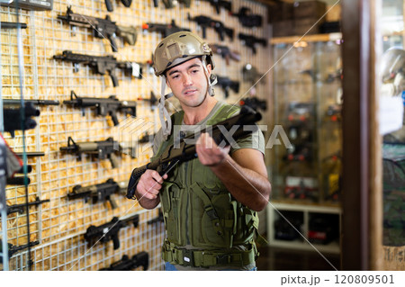 Man in armor vest selecting machine gun in air weapon shop 120809501