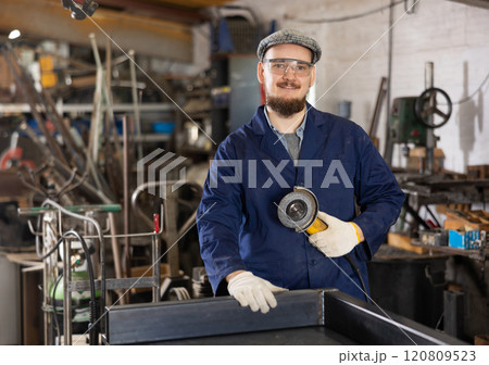 Portrait of positive mechanic with an angle grinder in his hands. Work at machine-building plant 120809523