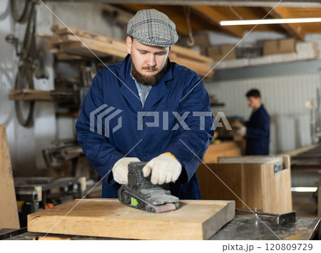 Young man polishing wooden board in workshop Young man polishing wooden board in workshop 120809729