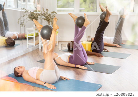 Students lying on floor, holding fitball in raised straight legs, rolling fitball in shins and feet Students lying on floor, holding fitball in raised straight legs, rolling fitball in shins and feet 120809825