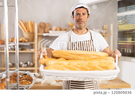 Caucasian male cook-baker worker with basket of baguettes, shows many products Caucasian male cook-baker worker with basket of baguettes, shows many products 120809836