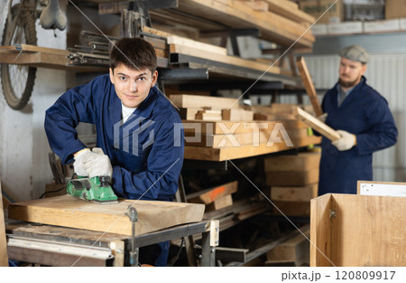 Young guy polishing wooden board in workshop 120809917