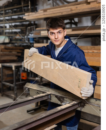 Young guy putting wooden board on cutting machine Young guy putting wooden board on cutting machine 120810005