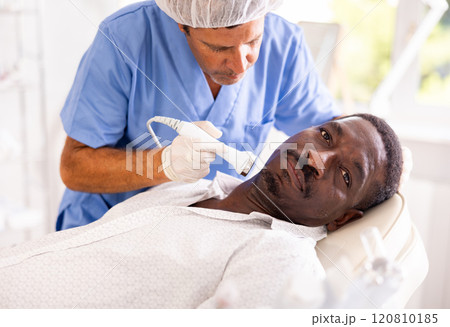 Male specialist uses ultrasonic import nozzle to care African man client face skin Male specialist uses ultrasonic import nozzle to care African man client face skin 120810185