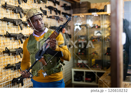 Man in armor vest selecting machine gun in weapon shop 120810232