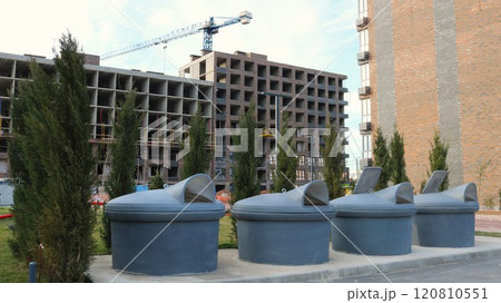 large closed containers for collecting and storing household waste in the courtyard of a modern residential complex against the backdrop of a high-rise building under construction large closed containers for collecting and storing household waste in the courtyard of a modern residential complex against the backdrop of a high-rise building under construction 120810551