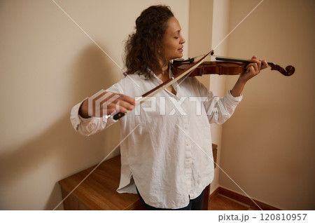 Woman playing violin with concentration in a cozy music room Woman playing violin with concentration in a cozy music room 120810957
