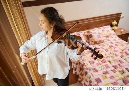 Young woman playing violin in cozy bedroom setting 120811014