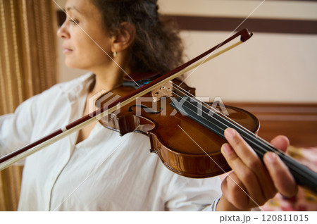 Close-up of woman playing violin in warmly lit room 120811015