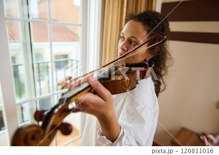 Young musician practicing violin near a sunlit window indoors 120811016