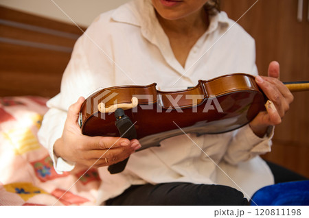 Woman tuning a violin in a cozy bedroom setting during daylight Woman tuning a violin in a cozy bedroom setting during daylight 120811198