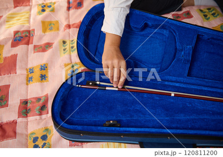 Hand placing a violin bow inside a blue velvet instrument case 120811200
