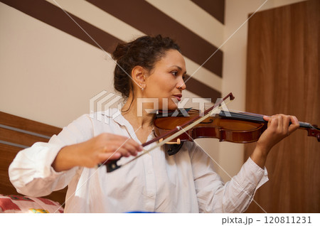 Woman playing violin in cozy room with striped wall decor Woman playing violin in cozy room with striped wall decor 120811231