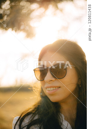 A woman wearing sunglasses. She is smiling and she is enjoying her walk. A woman wearing sunglasses. She is smiling and she is enjoying her walk. 120811438