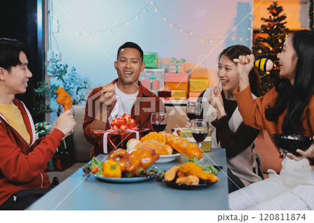 Group of young Asian man and women as friends having fun at a New Year's celebration, holding gift boxes standing by Christmas tree decoration, midnight countdown Party at home with holiday season. Group of young Asian man and women as friends having fun at a New Year's celebration, holding gift boxes standing by Christmas tree decoration, midnight countdown Party at home with holiday season. 120811874