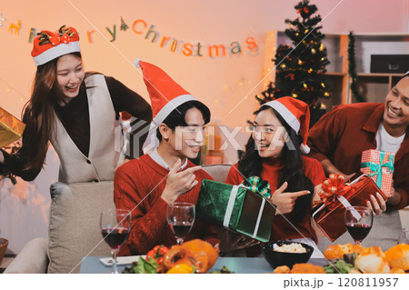 Group of young Asian man and women as friends having fun at a New Year's celebration, holding gift boxes standing by Christmas tree decoration, midnight countdown Party at home with holiday season. 120811957