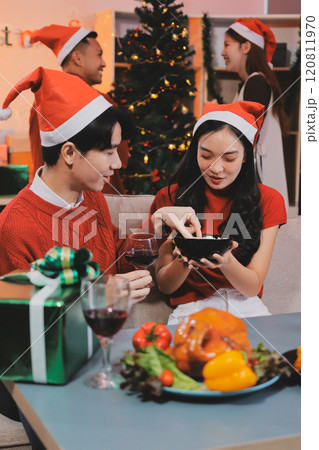 Group of young Asian man and women as friends having fun at a New Year's celebration, holding gift boxes standing by Christmas tree decoration, midnight countdown Party at home with holiday season. Group of young Asian man and women as friends having fun at a New Year's celebration, holding gift boxes standing by Christmas tree decoration, midnight countdown Party at home with holiday season. 120811970