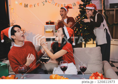 Group of young Asian man and women as friends having fun at a New Year's celebration, holding gift boxes standing by Christmas tree decoration, midnight countdown Party at home with holiday season. Group of young Asian man and women as friends having fun at a New Year's celebration, holding gift boxes standing by Christmas tree decoration, midnight countdown Party at home with holiday season. 120811973