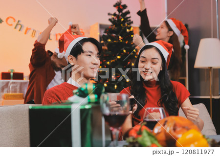 Group of young Asian man and women as friends having fun at a New Year's celebration, holding gift boxes standing by Christmas tree decoration, midnight countdown Party at home with holiday season. 120811977