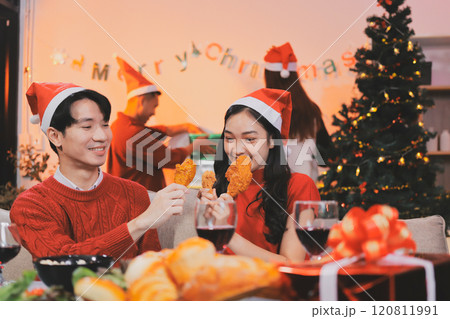 Group of young Asian man and women as friends having fun at a New Year's celebration, holding gift boxes standing by Christmas tree decoration, midnight countdown Party at home with holiday season. 120811991