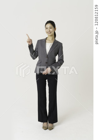 白背景のスーツを着た指差しをする若い女性の全身のポートレート　縦位置 120812159