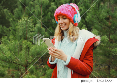 Happy young woman with phone listening to music in headphones in winter forest, Christmas tree Happy young woman with phone listening to music in headphones in winter forest, Christmas tree 120812221