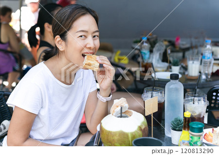 Happy asian woman eating tuna sandwich at local cafe outdoors. Happy asian woman eating tuna sandwich at local cafe outdoors. 120813290