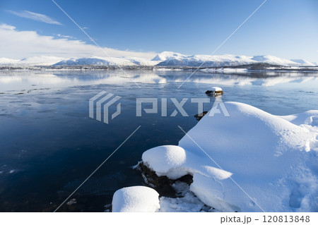 Snow covered coast of Norwegian fjord near Troms at Christmas time. A sunny winter day in Northern Norway above the Arctic Circle Snow covered coast of Norwegian fjord near Troms at Christmas time. A sunny winter day in Northern Norway above the Arctic Circle 120813848