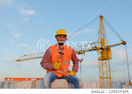 Construction worker sitting and holding hammer at construction site 120814304
