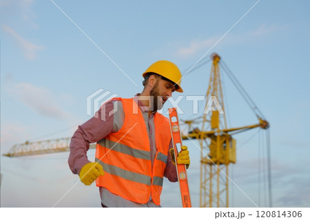 Construction worker wearing safety vest and holding spirit level at construction site Construction worker wearing safety vest and holding spirit level at construction site 120814306