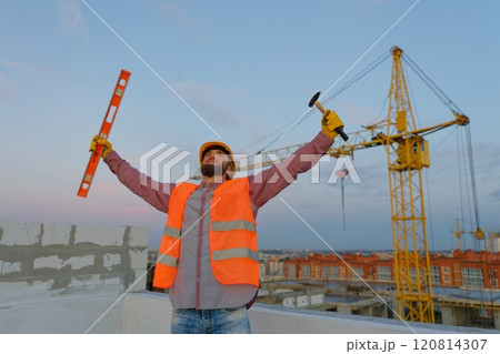 Construction worker celebrating with level and hammer at building site Construction worker celebrating with level and hammer at building site 120814307