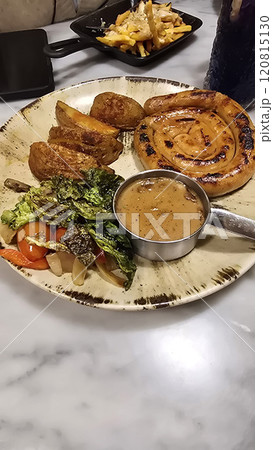 mouthwatering German worst curled up cumberland sausage meal featuring a grilled sausage, loaded cheese fries, and fresh vegetables served on a rustic plate mouthwatering German worst curled up cumberland sausage meal featuring a grilled sausage, loaded cheese fries, and fresh vegetables served on a rustic plate 120815130