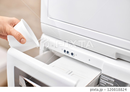 female hand pouring liquid laundry detergent from cap into washing machine, closeup 120818824