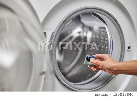 female hand putting capsule pod detergent for washing clothes into washing machine 120818840