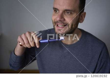 A 30-year-old man brushes his teeth with charcoal toothpaste using an electric toothbrush A 30-year-old man brushes his teeth with charcoal toothpaste using an electric toothbrush 120819192
