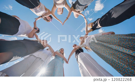 Group of friends joining hands forming heart shape against blue sky 120822268