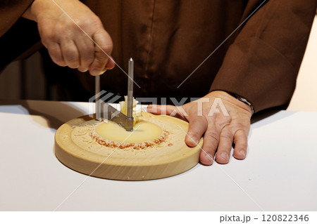 middle section of a middle aged man with hands in monk's robe cutting cheese 120822346