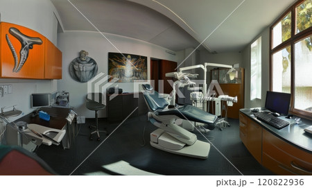 A minimalist dental office featuring a central dental chair, overhead LED light, and wall-mounted storage units. The space is designed with neutral tones and subtle green accents, creating a modern 120822936