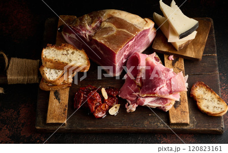 A piece of prosciutto, slices of ciabatta and cheese on a wooden board 120823161