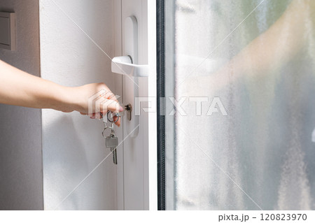 Hand on a door handle while turning a key to unlock a modern white door. 120823970