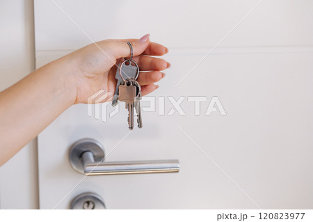 Person holding keys while locking or unlocking a white door, close-up shot 120823977
