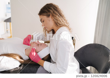 A beautician applies a facial mask with precision using a brush, highlighting a professional skincare routine A beautician applies a facial mask with precision using a brush, highlighting a professional skincare routine 120824006