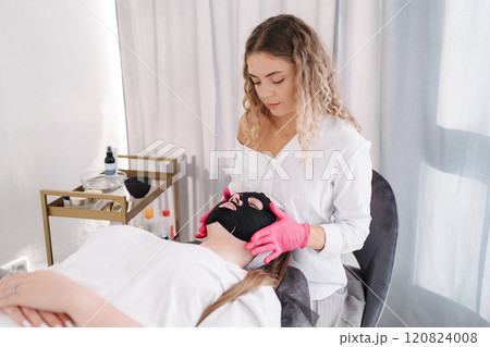 Aesthetician applies a hydrating mask to the face, deeply nourishing the skin and restoring its natural softness and elasticity Aesthetician applies a hydrating mask to the face, deeply nourishing the skin and restoring its natural softness and elasticity 120824008