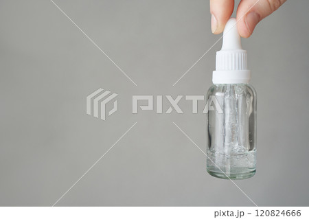 Hand holding clear dropper bottle with liquid against gray background 120824666