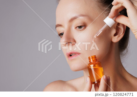 Happy smiling woman applying serum on her face, close eyes with pleasure. Redhead girl holding dropper with skin care product for healthy and glowing skin tone Happy smiling woman applying serum on her face, close eyes with pleasure. Redhead girl holding dropper with skin care product for healthy and glowing skin tone 120824771