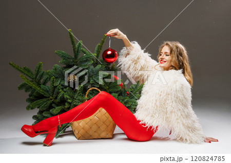 sexy woman in red tights and high heels lying near christmas tree holding red decoration in hands, fashion christmas 120824785