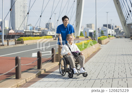屋外で車椅子を押す介護スタッフ 120825229