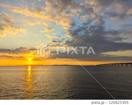 Rinku Town, Japan - 08.12.2024: Sunset at Osaka Bay with Kansai Internation Aiport at the horizon connected by a bridge at the golden hour under a blue and golden gradient sky and dramatic clouds Rinku Town, Japan - 08.12.2024: Sunset at Osaka Bay with Kansai Internation Aiport at the horizon connected by a bridge at the golden hour under a blue and golden gradient sky and dramatic clouds 120825305