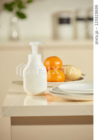 Mockup for advertising of cleaning products in the context of the kitchen. A bottle without brand is placed in the corner of the kitchen island, besides some fresh fruits and white porcelain plates 120828686