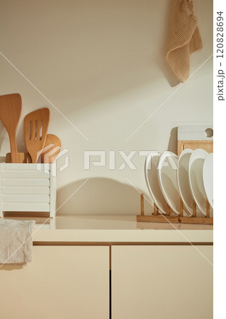 Front view photograph in minimalist kitchen. Wooden dishes and cooking utensils are featured on the beige kitchen counter, which is placed close to the wall, vacant space in center for product placing 120828694